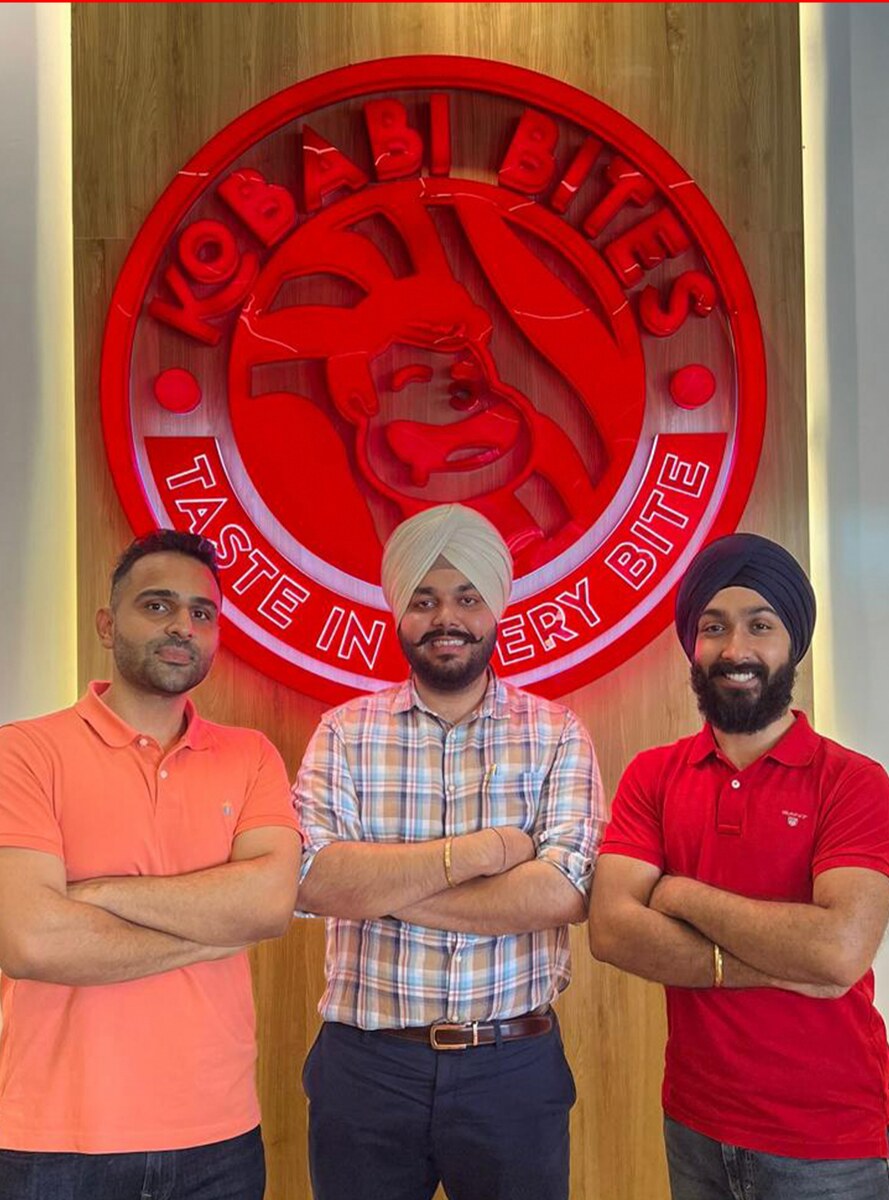 The three founders in front of the outlet's neon logo wall