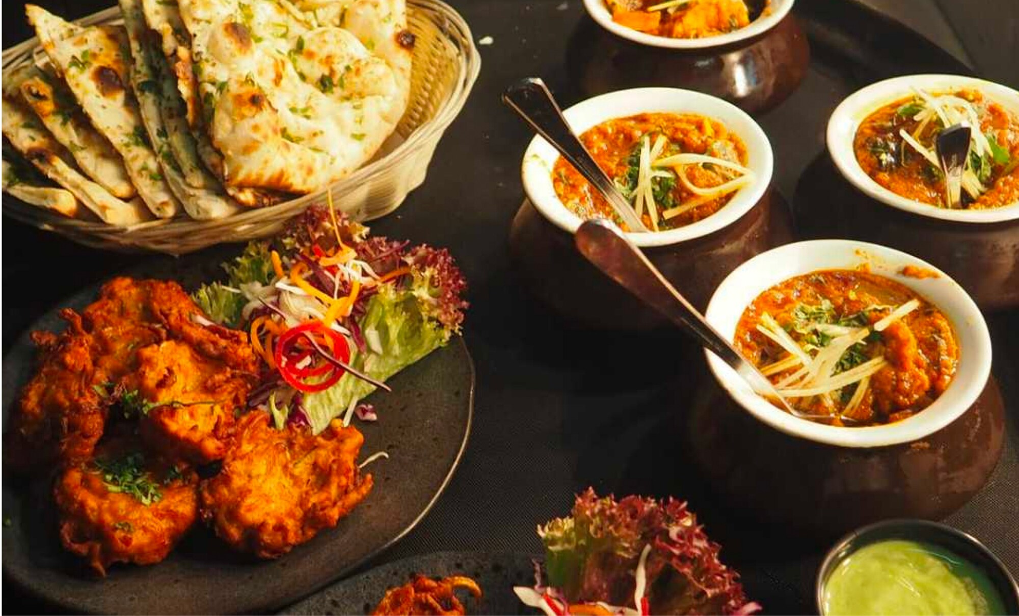Fresh naan beside bowls of North Indian gravy topped with ginger
